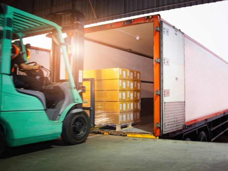 Forklift Driver Loading Package Boxes into Cargo Container. Cargo Trailer Truck Parked Loading at Dock Warehouse. Shipment Delivery Service. Shipping Warehouse Logistics. Freight Truck Transportation.